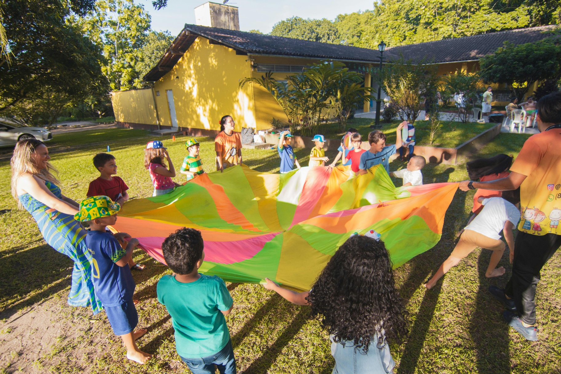Voluntárias e crianças brincando juntas com paraquedas colorido ao ar livre